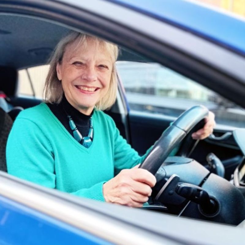 Volunteer driver sitting and smiling in the driving seat of her car